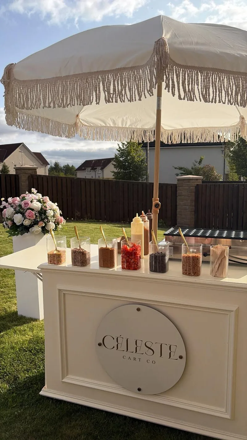 The Céleste cart with fringed parasol and flowers in a garden